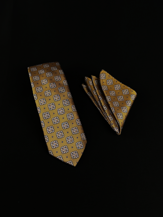 A yellow necktie and matching pocket square set with a repeating geometric medallion pattern in gray, white, and teal.