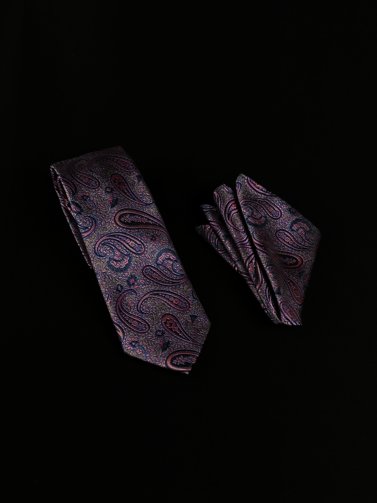 A matching necktie and pocket square set with a detailed paisley pattern in pink, blue, and red tones.