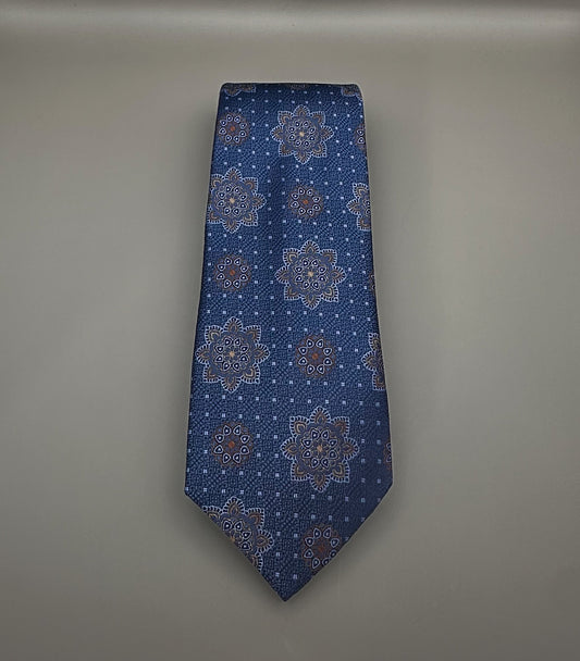 A classic necktie with a deep blue base and a detailed geometric medallion pattern in light blue, dark blue and tan.