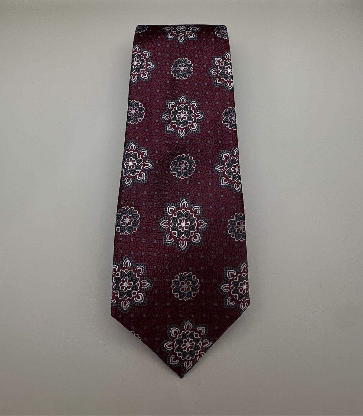 A classic necktie with a deep burgundy base and a detailed geometric medallion pattern in light gray, dark gray, and burgundy.